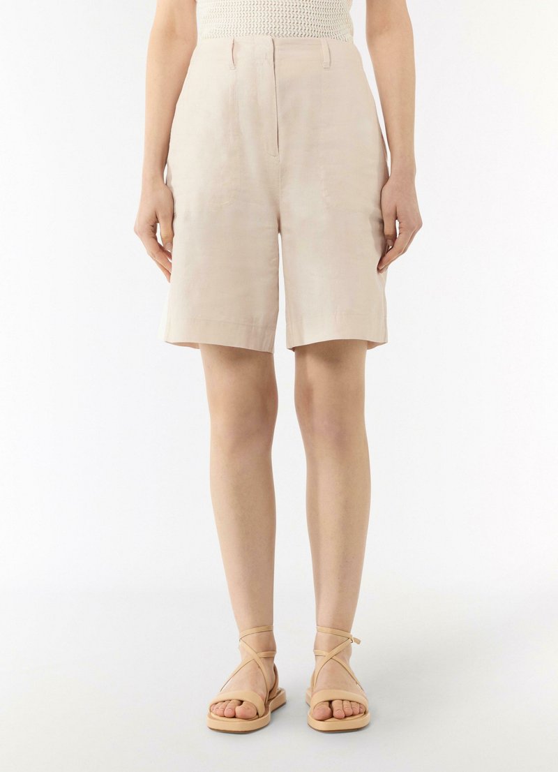 Light beige linen shorts with a relaxed fit, folded hem, front pockets, and a zipper closure. Paired with beige strappy sandals.