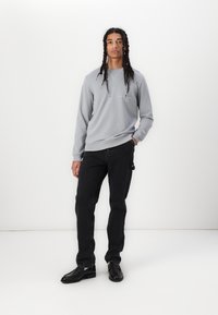 Grauer Sweatshirt mit Rundhalsausschnitt, gerippten Bündchen und einem einfachen Logo. Getragen mit schwarzen Jeans und schwarzen Schuhen. Glattes Material und lässige Passform.