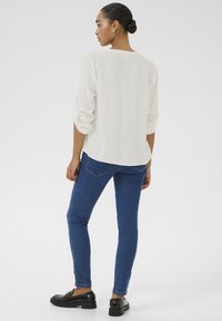 Blusa a maniche lunghe color avorio con vestibilità ampia e maniche arrotolate, abbinata a jeans attillati blu scuro e mocassini neri. Tessuto liscio, stile casual.