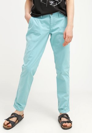 Lichtblauwe katoenen broek met een slim fit, voorzien van standaardzakken en subtiele zijsplitten bij de enkels. Gemaakt in combinatie met zwarte sandalen.