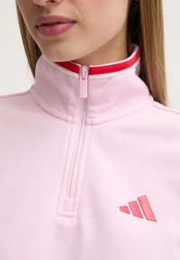 Pullover rosa con zip e colletto alto, con colletto e zip di accento rossi, tessuto testurizzato e logo rosa sul petto.