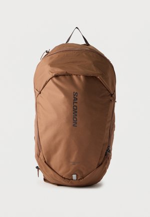 Rucsac maro Salomon Trailblazer 20L cu mâner superior, buzunare frontale cu fermoar și logo vertical negru pe un fundal simplu.