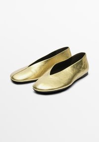 Guldläderballetskor med en slät yta, en v-formad öppning framtill och en låg, platt svart sula.