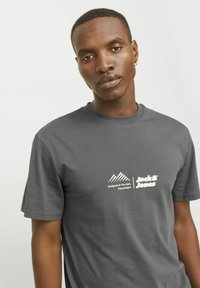 Grå bomulds T-shirt med rund hals, korte ærmer og et grafisk logo i hvid, der inkluderer bjerge og tekst, på brystet.
