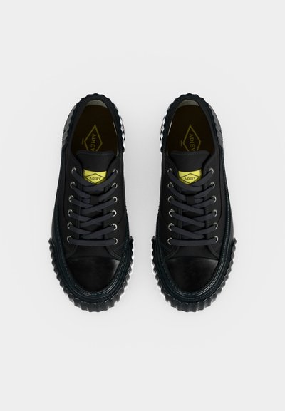 Paire de baskets basses noires à lacets avec semelle texturée et étiquette jaune à l'intérieur, vues de dessus sur fond blanc.