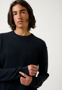 Pull en tricot bleu marine avec un col rond, coupe décontractée et manches longues. Texture douce, détails minimalistes et poignets côtelés.