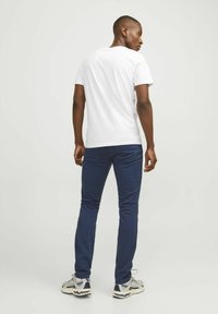 Biele krátke tričko s okrúhlym výstrihom, skombinované s námornícky modrými slim-fit nohavicami a šedými športovými topánkami. Minimalistický dizajn, bez viditeľných vzorov.