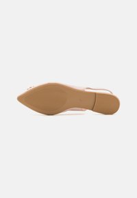 Sandalia de tacón con upper de charol nude y puntera afilada. Presenta una suela de goma beige texturizada y sutiles acentos decorativos.