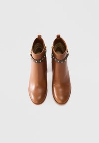 Pair of brown leather ankle boots with round toes, gold studs on dark straps around the top, and inner side zippers on white background.