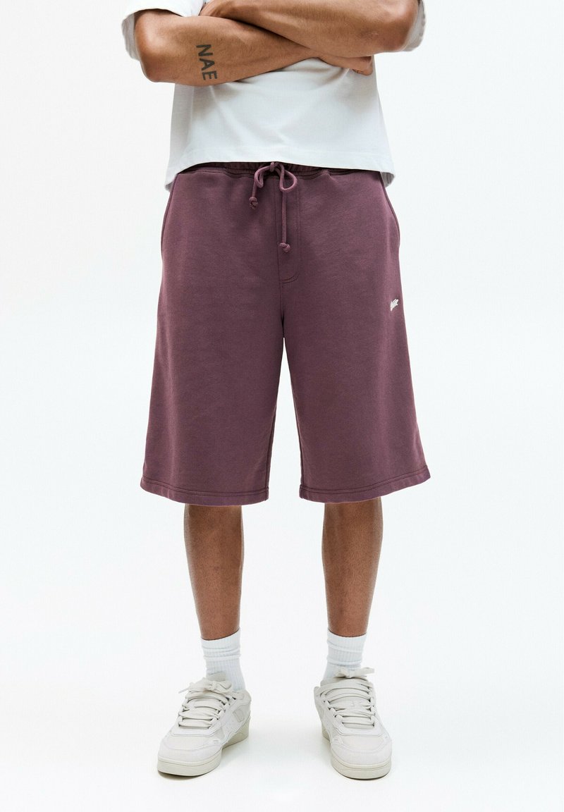 Shorts violets en tissu doux avec une taille élastique et un cordon de serrage. Comprend des poches latérales et un petit logo blanc à l'avant.