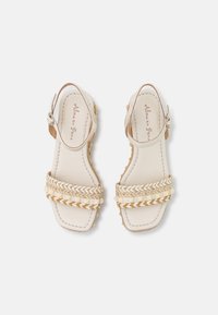 Sandali in pelle bianca con cinturini intessuti in beige e marrone chiaro. Forma della punta arrotondata, cinturino alla caviglia con fibbia e dettagli testurizzati sulla suola.