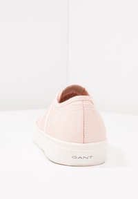 Baskets en toile rose pâle vues de l'arrière, semelle en caoutchouc blanche avec étiquette "GANT" sur le talon, sur une surface et un fond blancs.