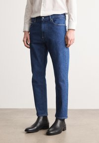 Jeans de mezclilla azul con un corte recto, que presentan un diseño clásico de cinco bolsillos, costuras amarillas y se llevan con botines negros.