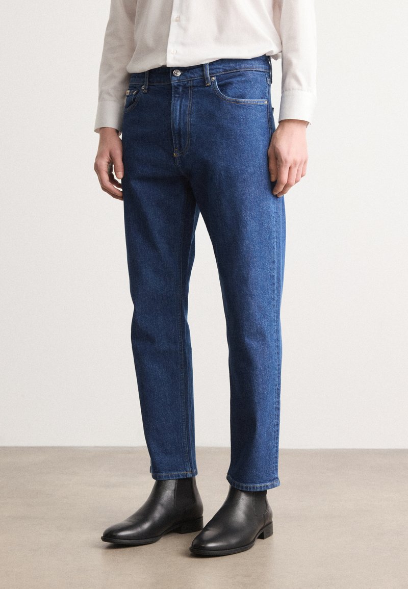 Jeans de mezclilla azul con un corte recto, que presentan un diseño clásico de cinco bolsillos, costuras amarillas y se llevan con botines negros.