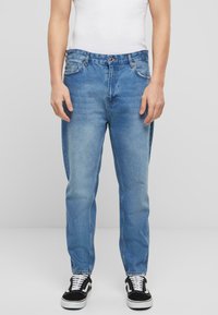Jeans de mezclilla azul claro de corte recto, con cinco bolsillos, pasadores para cinturón y un deslavado sutil. Llevados con zapatillas negras y blancas.