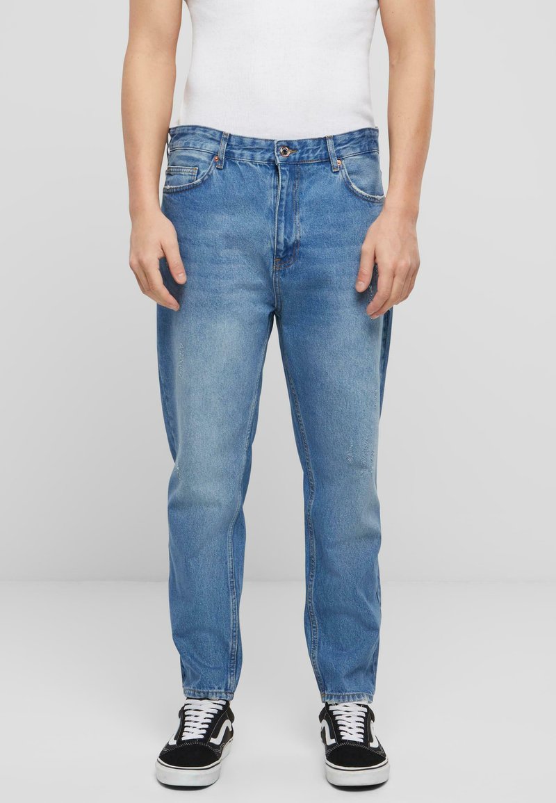 Jeans de mezclilla azul claro de corte recto, con cinco bolsillos, pasadores para cinturón y un deslavado sutil. Llevados con zapatillas negras y blancas.