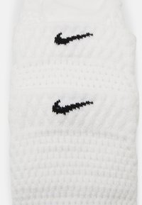 Valkoiset puuvillaiset rannekkeet, joissa on teksturoitu kuvio, ja jokainen on koristeltu pienellä mustalla Nike-logolla ommeltuna eteen.