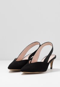 Černé semišové slingback podpatky s špičatou špičkou, otevřenou patou a tkanými detaily pásku. Úzký stiletto podpatek a béžová vnitřní podšívka.