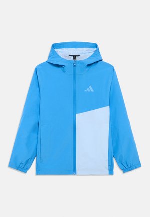 Jachetă windbreaker albastră cu un panou albastru deschis, prevăzută cu glugă, închidere cu fermoar și manșete elastice. Sigla Adidas în albastru deschis pe piept.