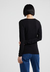 Schwarzes Langarmoberteil mit rundem Halsausschnitt und taillierter Passform, kombiniert mit blauen Jeans aus Denim mit heller Waschung und klassischen Gesäßtaschen.
