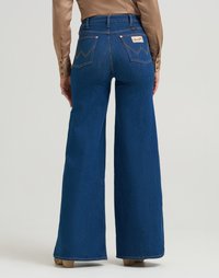 Jeans in denim a gamba larga di colore blu scuro. Presentano una vita alta, cuciture in contrasto e un design unico della tasca posteriore con etichetta del marchio.