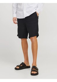 Pantalones cortos negros con bolsillos laterales, hechos de una tela ligera, combinados consandalias negras tipo deslizamiento con correas ajustables y una suela plana.