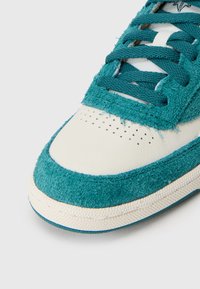 Κοντινό πλάνο από μπλε σουέντ και λευκό δερμάτινο παπούτσι αθλητικών με perforations και μπλε κορδόνια σε άσπρο φόντο.