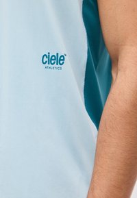 Αθλητικό αμάνικο μπλουζάκι ανοιχτού γαλάζιου χρώματος με το λογότυπο "ciele ATHLETICS" στο στήθος, φορεμένο από ένα άτομο που δείχνει μέρος του βραχίονα του.