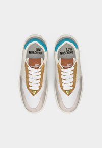 Ζευγάρι λευκών αθλητικών παπουτσιών Love Moschino με καφέ, μπεζ και μπλε λεπτομέρειες, λευκά κορδόνια και χρυσά κρεμαστά καρδιές στα δάχτυλα.
