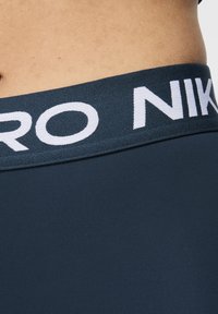 Fascia elastica blu navy con logo bianco "NIKE". Tessuto liscio, design aderente che mostra parzialmente la pelle sottostante.