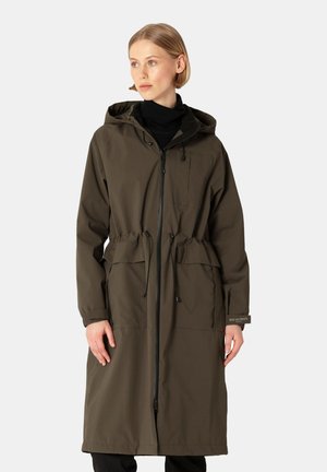 Woman wearing a long olive green hooded coat with front zipper and drawstring waist, standing against a light gray background.