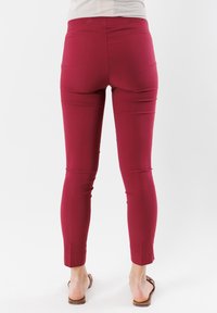 Vista posteriore di pantaloni aderenti color bordeaux realizzati in un tessuto morbido e elasticizzato. L'orlo è accorciato appena sopra la caviglia e la vita è senza cuciture.