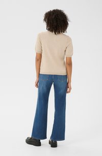 Beige kortekous top gecombineerd met wijde blauwe jeans. De jeans hebben twee achterzakken en een lichte rafeling aan de Zoom. Zwarte chunky schoenen.