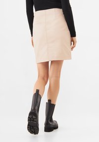 Světle béžová tužková sukně s hladkou strukturou, délky po kolena, se středovým švem, spárovaná s černými kotníkovými botami s texturovanou podrážkou.