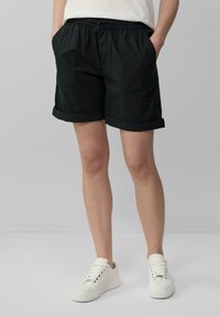 Pantalones cortos negros, ligeros, con cintura elástica y dobladillos enrollados, que cuentan con bolsillos laterales. Combinados con zapatillas blancas sobre un fondo neutro.
