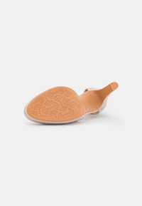 Beige suede shoe with a pointed toe and open back. The sole features an embossed floral pattern, providing grip and texture.