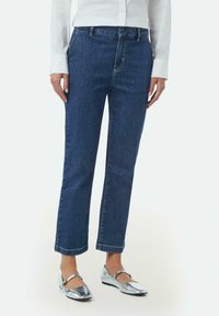 Donkerblauwe denim jeans met een recht model, voorzien van voorzakken en een knoopsluiting. Accentuatie met opgerolde zoom voor een casual uitstraling.
