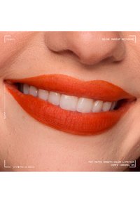 Close-up of a smiling mouth with bright orange matte lipstick applied smoothly on the lips showing natural skin texture.