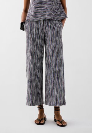 Pantaloni a gamba larga in tessuto a righe multicolori, con una superficie texturizzata e tasche laterali. Abbinati a sandali neri con cinturini.
