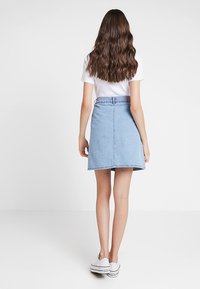 Denimkjol i ljusblå färg, A-linjeformad och med midjeband. Stylad med en vit t-shirt och vita sneakers. Bakåtsikt visad.