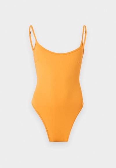 Φωτεινό πορτοκαλί ολόσωμο μαγιό με λεπτές ρυθμιζόμενες τιράντες σε μονόχρωμο ανοιχτό γκρι φόντο.