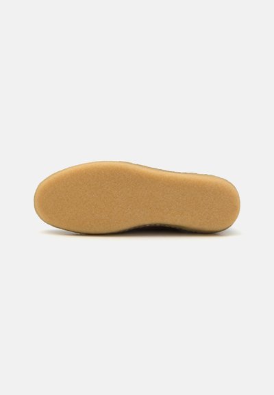 Sole of a shoe featuring a smooth, light brown rubber base with a textured surface for grip, tapering towards the toe.