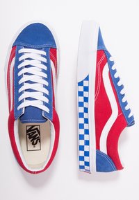 Tenisky Vans v červené a modré plátno, bílé akcenty, modrý kostkovaný vzor na podrážce a bílé tkaničky. Klasický nízký design.