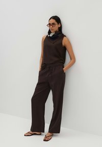 Donkerbruine mouwloze top en losse broek met een trekkoord in de taille. Aangevuld met een patroon sjaal en minimalistische sandalen.