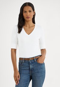 Balts V veida izgriezuma tops ar trīs ceturtdaļu piedurknēm, kombinēts ar zilām džinsa biksēm. Ievērības cienīgs ir brūns josta ar metāla logotipa sprādzi.