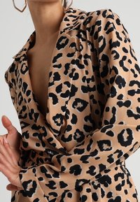 Halenka s leopardím vzorem v béžové a černé barvě, se límečkem, dlouhými rukávy a zavinovacím designem, s hladkou texturou a splývavou látkou.