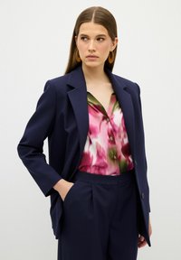 Námořnický blazer se strukturovanými klopami, doplněný barevnou blůzou s květinovým potiskem v růžových a zelených odstínech a ladícími kalhotami na míru.