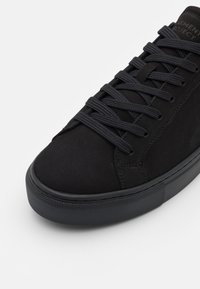 Svart mockaskor med avrundad tå, platt gummisula och matchande snörning. Har en minimalistisk design med en texturerad ovandel och ett varumärkesdetalj.