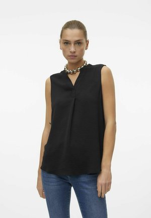 Schwarzes ärmelloses Oberteil mit V-Ausschnitt, aus strukturiertem Stoff. Getragen mit blauen Jeans und einer massiven metallischen Halskette.