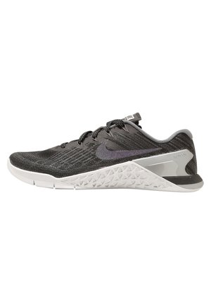 Nike training shoes with a textured black knit upper, contrasting gray rubber sole, and a geometric textured heel. Features laces and logo.